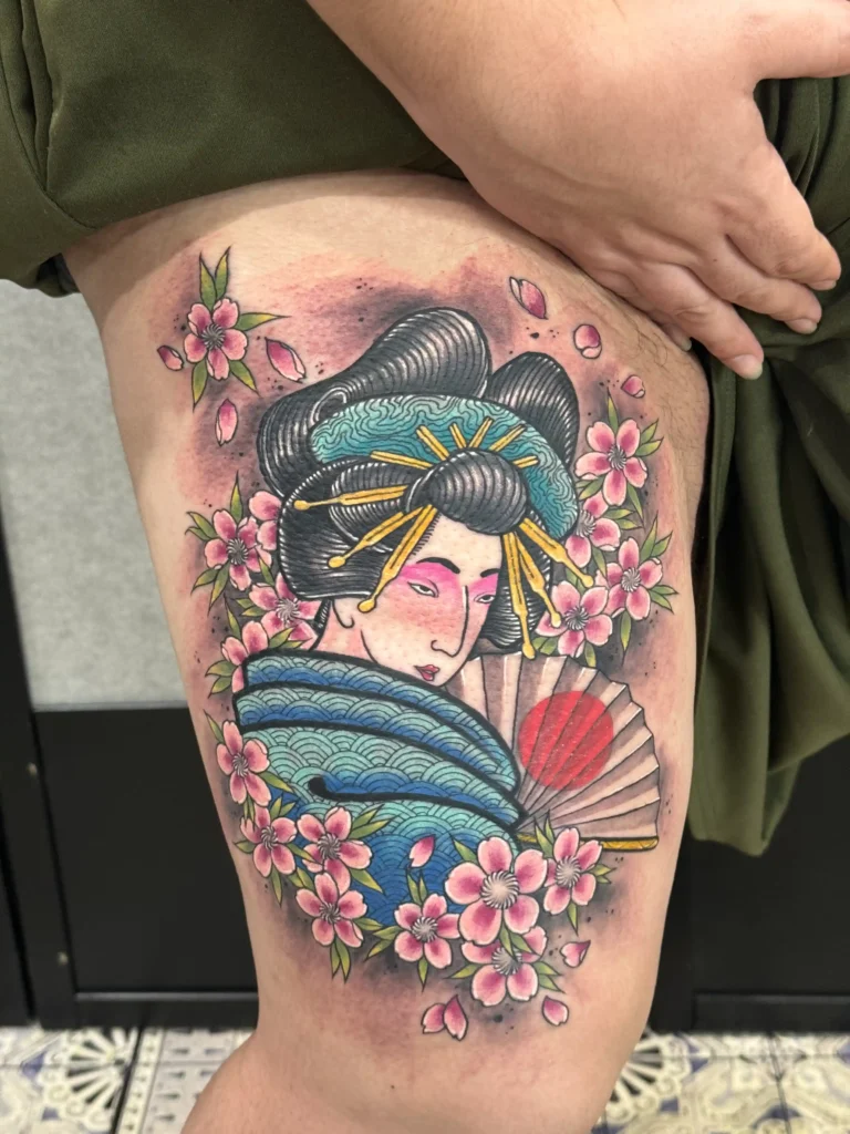 Colorful Japanese tattoo on leg of geisha with fan and sakura flowers, done in Tokyo by Mangesh Rane – traditional irezumi design symbolizing beauty and grace | tattoointokyo